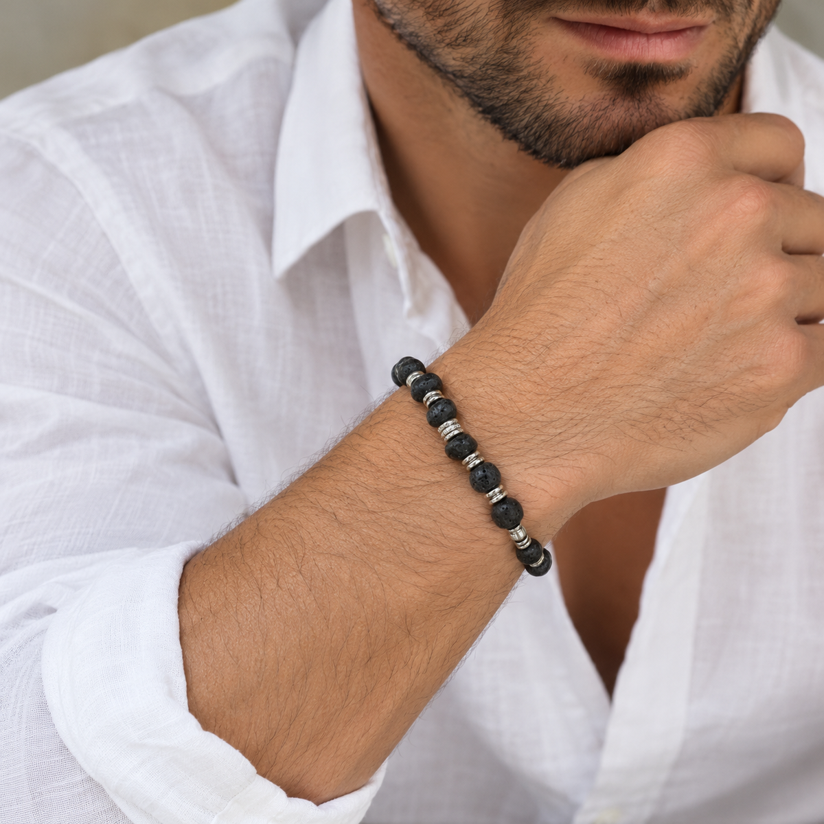 Bracciale elastico in pietra lavica nera con separatori in acciaio, indossato con camicia di lino bianca