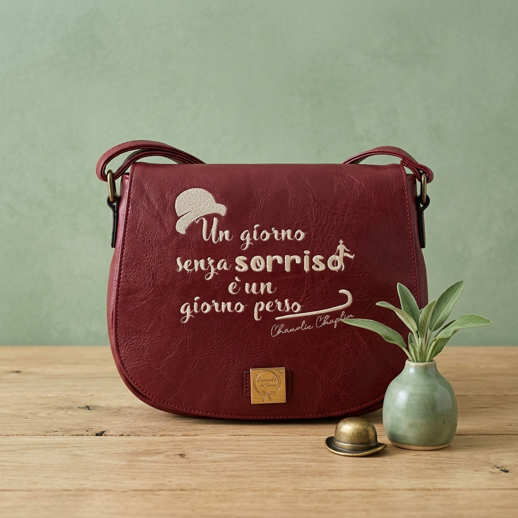 Borsa in ecopelle bordeaux con ricamo artigianale "Un giorno senza sorriso è un giorno perso" di Charlie Chaplin e dettaglio bombetta, 27x20cm