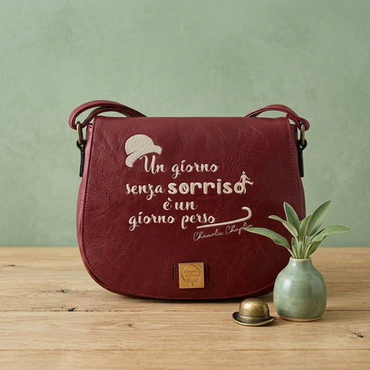 Borsa in ecopelle bordeaux con ricamo artigianale "Un giorno senza sorriso è un giorno perso" di Charlie Chaplin e dettaglio bombetta, 27x20cm